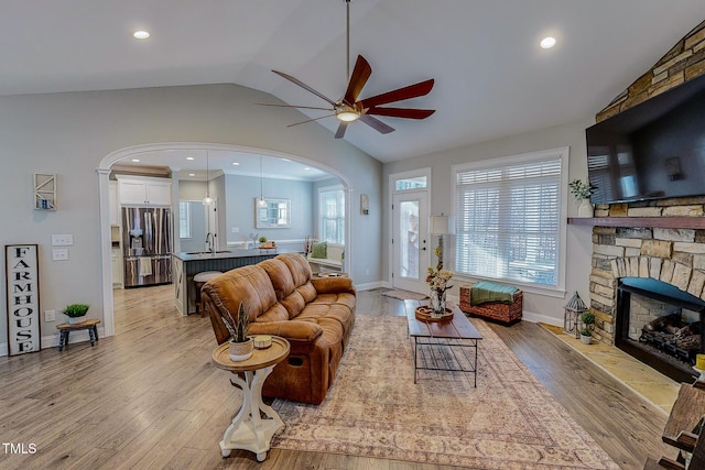 living room featuring lofted ceiling, sink, a stone fireplace, and light hardwood / wood-style flooring