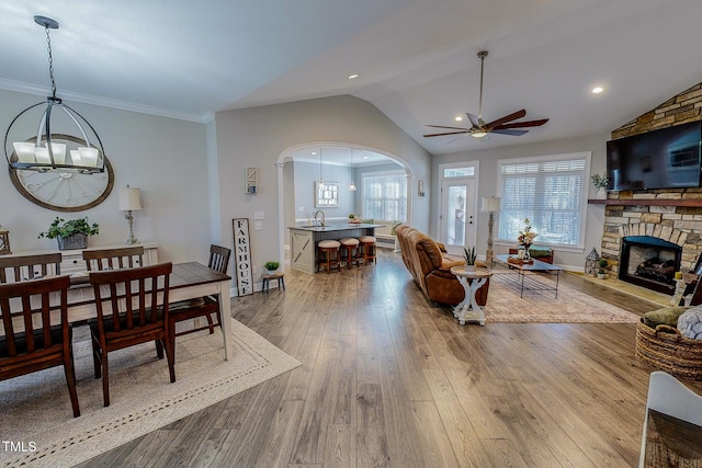 living room with vaulted ceiling, a stone fireplace, sink, crown molding, and light wood-type flooring