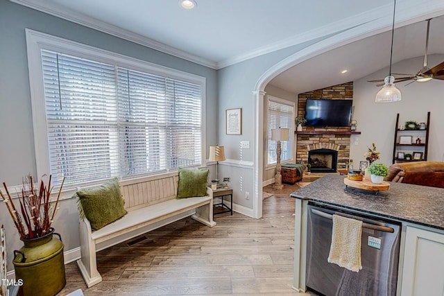 kitchen featuring a stone fireplace, vaulted ceiling, light hardwood / wood-style flooring, stainless steel dishwasher, and white cabinets