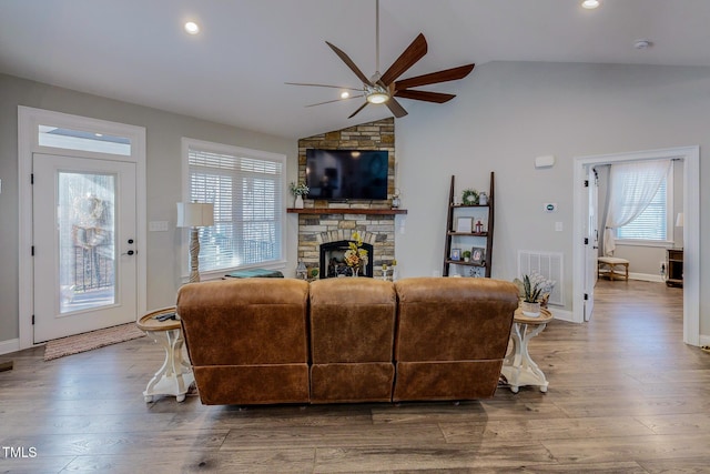 living room featuring vaulted ceiling, ceiling fan, a stone fireplace, and hardwood / wood-style floors