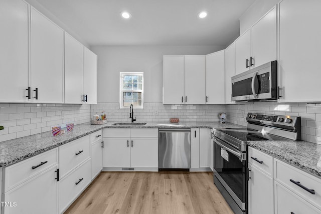 kitchen with stainless steel appliances, sink, white cabinets, and light stone counters