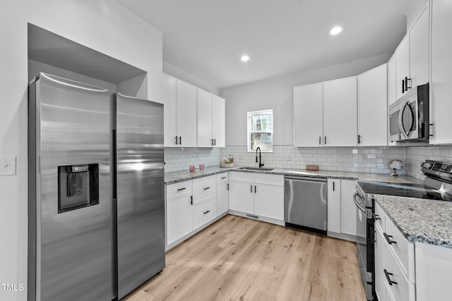 kitchen with sink, white cabinetry, light stone counters, stainless steel appliances, and backsplash