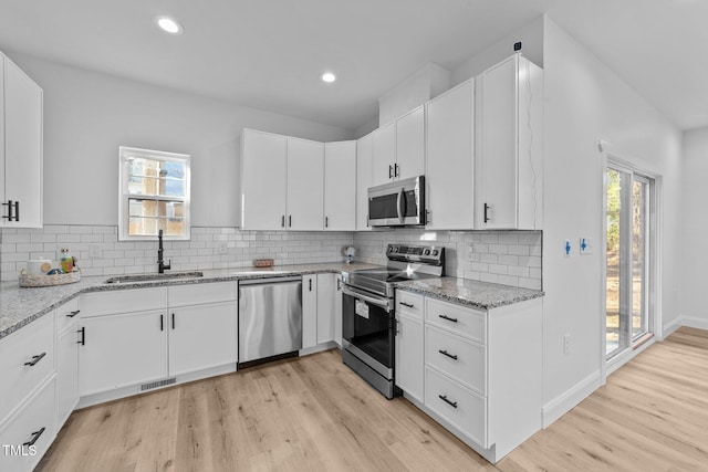 kitchen with sink, light hardwood / wood-style flooring, stainless steel appliances, light stone countertops, and white cabinets