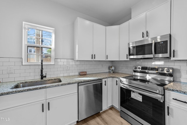 kitchen with sink, white cabinetry, stainless steel appliances, light stone countertops, and decorative backsplash