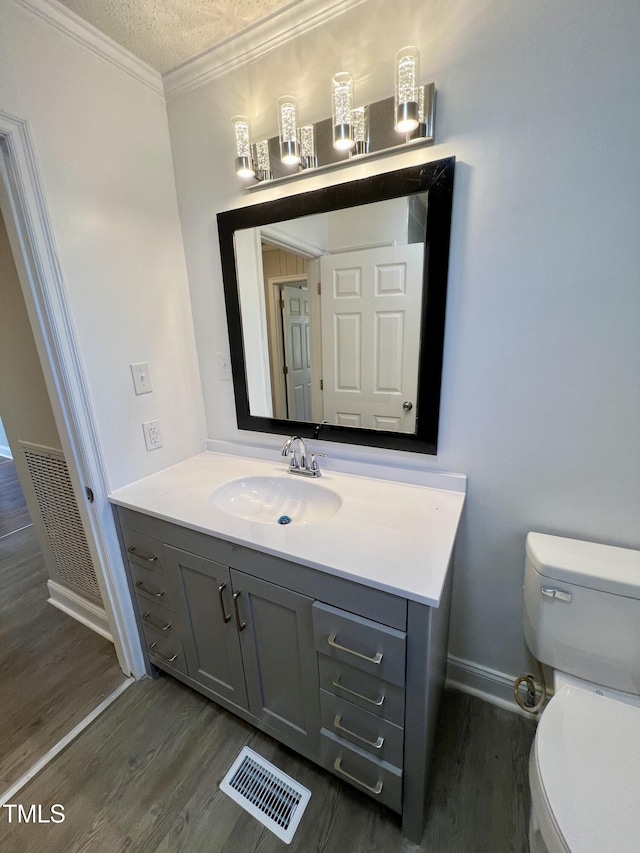 bathroom featuring hardwood / wood-style floors, ornamental molding, vanity, toilet, and a textured ceiling