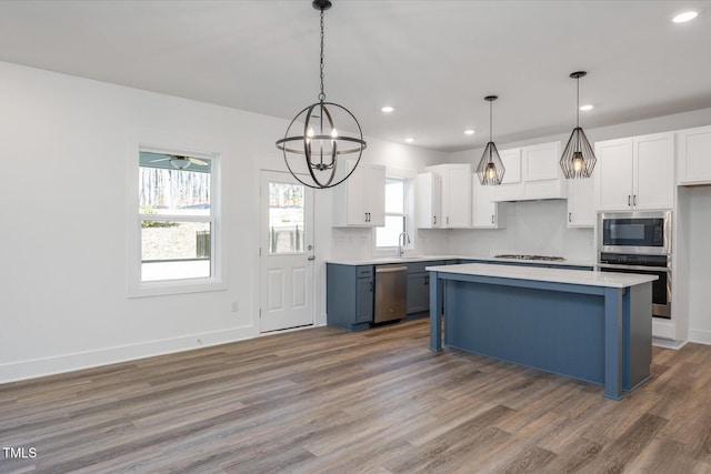 kitchen with blue cabinets, hanging light fixtures, white cabinets, and appliances with stainless steel finishes