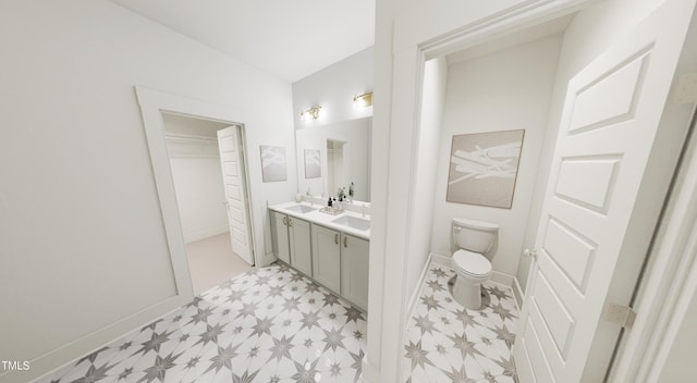 bathroom featuring a walk in closet, double vanity, toilet, a sink, and tile patterned floors