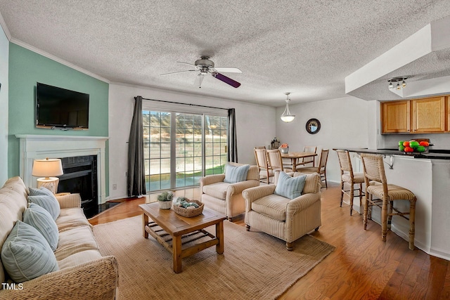 living room featuring a textured ceiling, light hardwood / wood-style flooring, ornamental molding, and ceiling fan