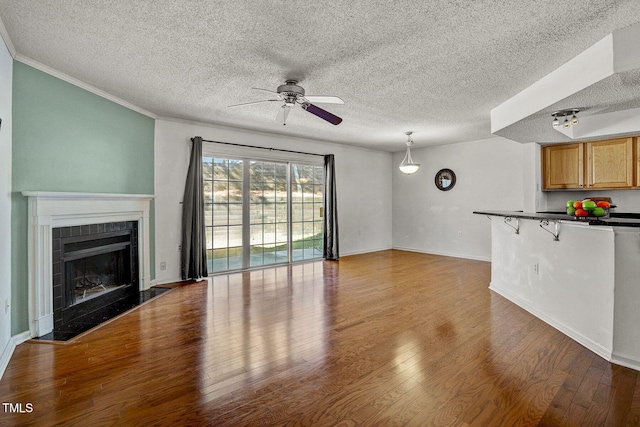 unfurnished living room featuring ceiling fan, hardwood / wood-style floors, a tile fireplace, and a textured ceiling