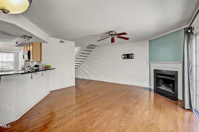 unfurnished living room with a fireplace, ceiling fan, light hardwood / wood-style floors, crown molding, and a textured ceiling