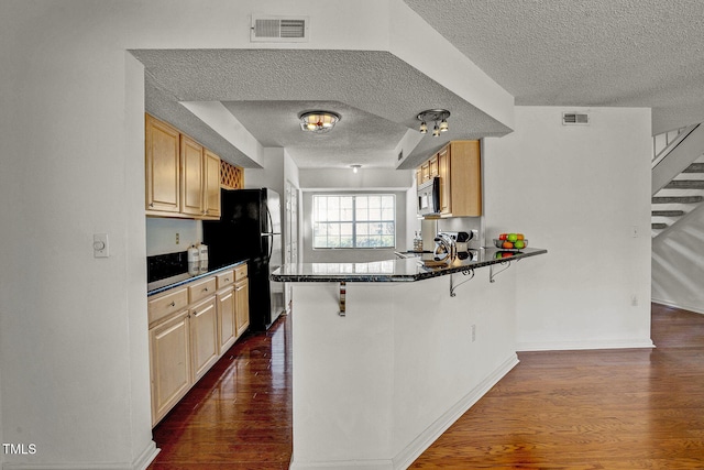 kitchen with black appliances, dark hardwood / wood-style flooring, a kitchen bar, and kitchen peninsula