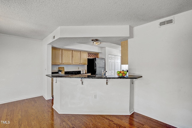 kitchen with black fridge, a kitchen bar, kitchen peninsula, and dark wood-type flooring