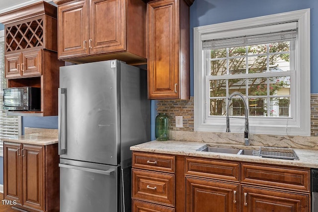 kitchen with light stone counters, sink, backsplash, and stainless steel fridge