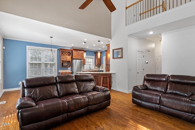 living room with hardwood / wood-style flooring, ornamental molding, ceiling fan, and a towering ceiling