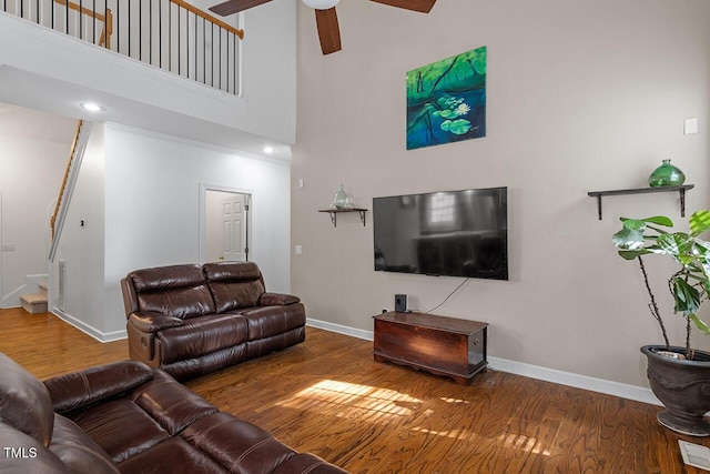 living room featuring hardwood / wood-style flooring, ceiling fan, and a towering ceiling