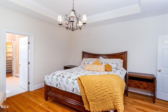 bedroom featuring a raised ceiling, crown molding, and light wood-type flooring