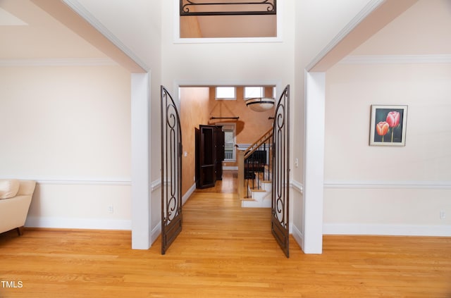 entrance foyer featuring a towering ceiling, ornamental molding, and light wood-type flooring