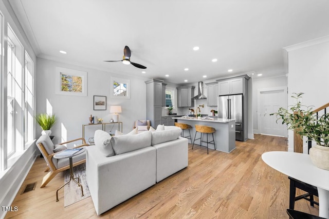 living room with crown molding, ceiling fan, sink, and light hardwood / wood-style flooring