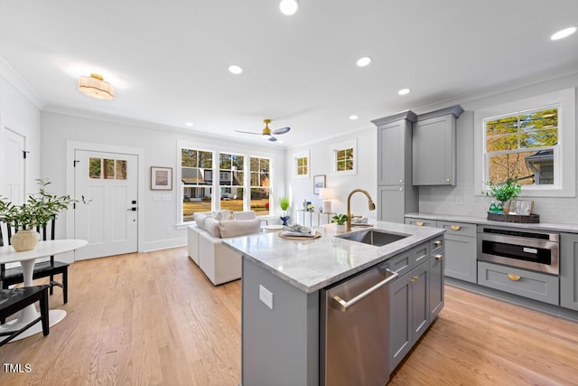 kitchen with sink, crown molding, appliances with stainless steel finishes, light stone counters, and a center island with sink