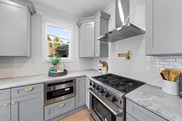 kitchen featuring gray cabinets, wall chimney range hood, stainless steel range, and light stone counters