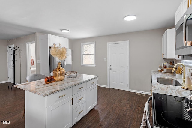 kitchen featuring appliances with stainless steel finishes, sink, white cabinets, light stone countertops, and dark wood-type flooring