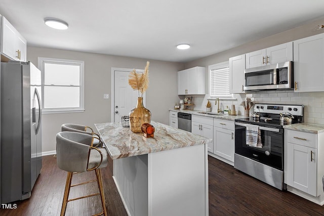 kitchen with appliances with stainless steel finishes, white cabinetry, sink, a center island, and light stone countertops