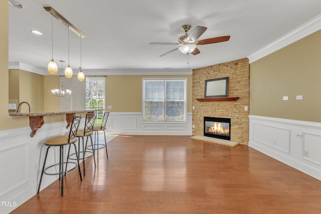 living area with a fireplace, crown molding, wood finished floors, and ceiling fan with notable chandelier