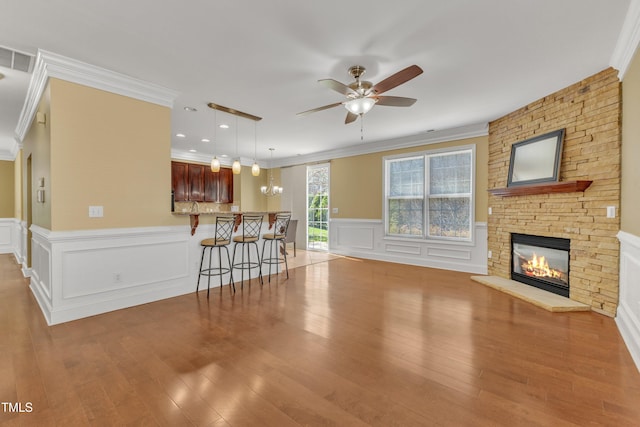 living room with wood finished floors, a fireplace, ceiling fan, crown molding, and a decorative wall