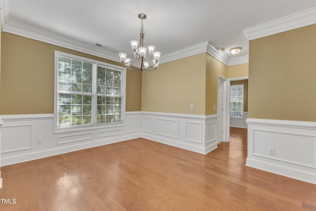 unfurnished room featuring a notable chandelier, light wood-style floors, wainscoting, and ornamental molding