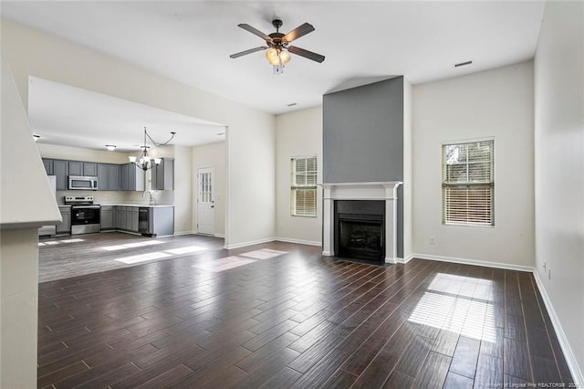 unfurnished living room with dark hardwood / wood-style flooring, sink, and ceiling fan with notable chandelier