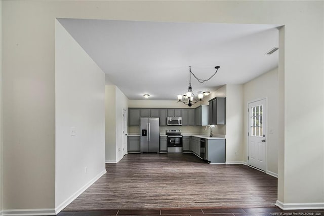 kitchen featuring gray cabinets, appliances with stainless steel finishes, hanging light fixtures, dark wood-type flooring, and an inviting chandelier