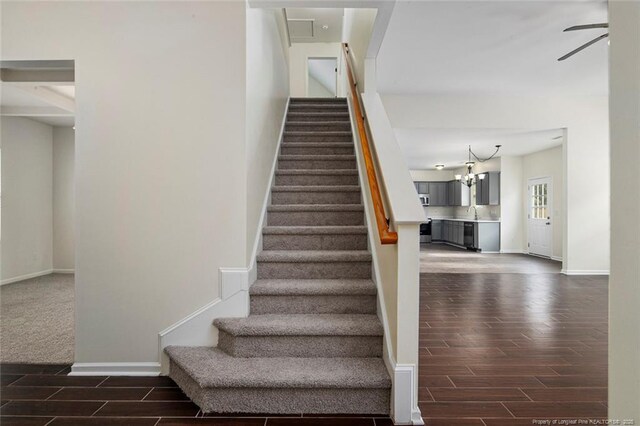 stairs featuring ceiling fan with notable chandelier