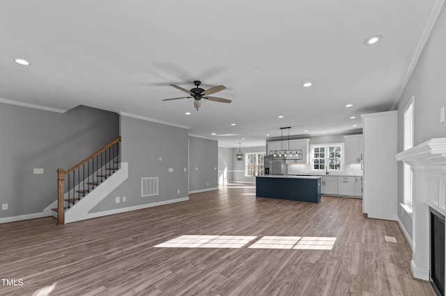 unfurnished living room with sink, ornamental molding, ceiling fan, and light wood-type flooring