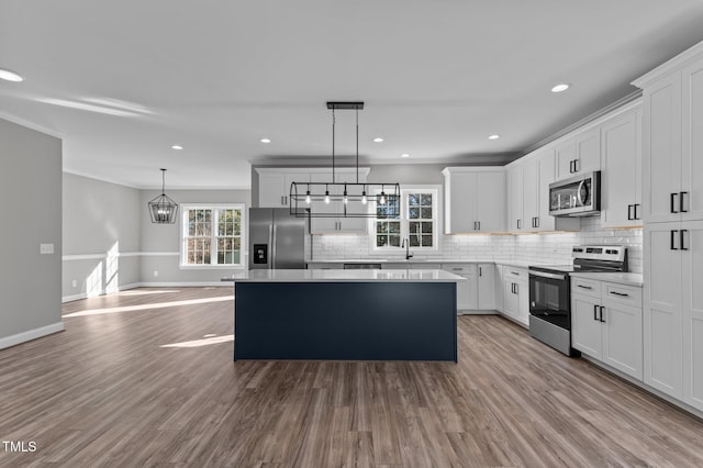 kitchen with crown molding, hanging light fixtures, appliances with stainless steel finishes, a kitchen island, and white cabinets