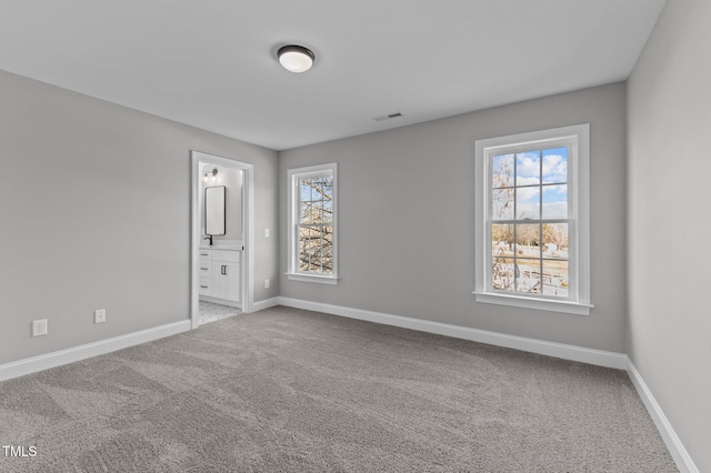 unfurnished bedroom with multiple windows, ensuite bathroom, and carpet flooring