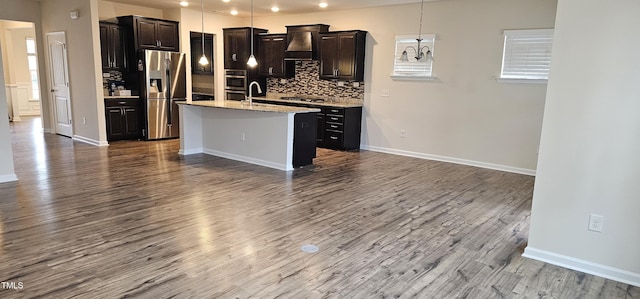 kitchen featuring light stone counters, wood-type flooring, decorative light fixtures, a center island with sink, and appliances with stainless steel finishes