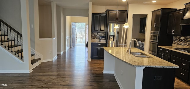 kitchen with sink, appliances with stainless steel finishes, dark hardwood / wood-style floors, light stone countertops, and a center island with sink