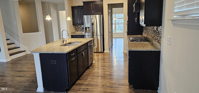 kitchen with pendant lighting, an island with sink, sink, stainless steel appliances, and light stone countertops