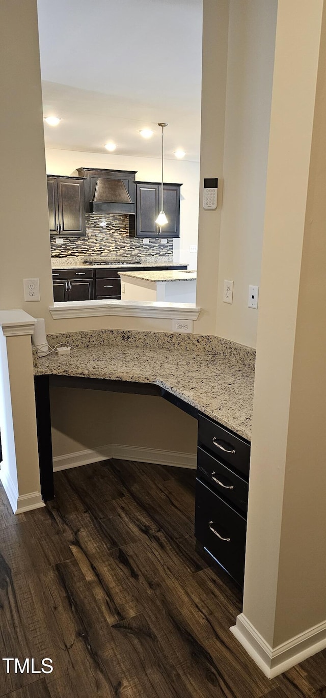 kitchen featuring built in desk, pendant lighting, dark hardwood / wood-style flooring, light stone countertops, and wall chimney exhaust hood