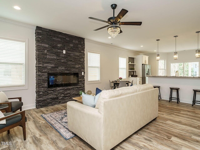 living room featuring ceiling fan, ornamental molding, a stone fireplace, and light wood-type flooring