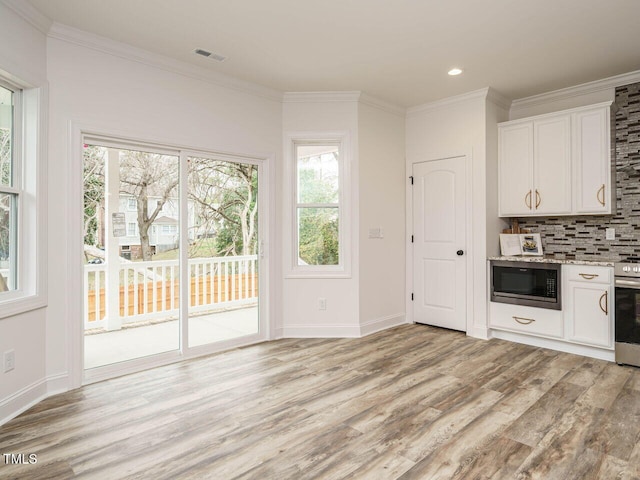 kitchen with built in microwave, white cabinetry, tasteful backsplash, and light wood-type flooring