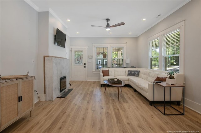 living room with crown molding, a high end fireplace, light hardwood / wood-style floors, and ceiling fan