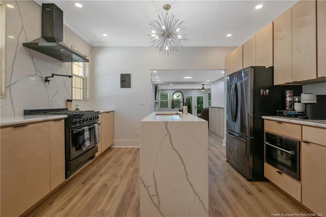 kitchen with wall chimney exhaust hood, sink, hanging light fixtures, light brown cabinets, and black appliances