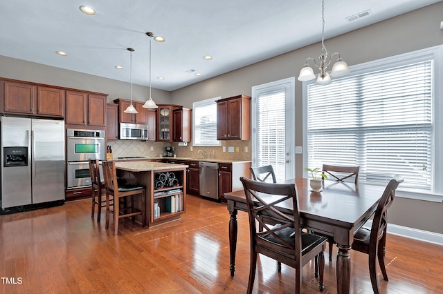 kitchen with appliances with stainless steel finishes, a center island, glass insert cabinets, and hanging light fixtures