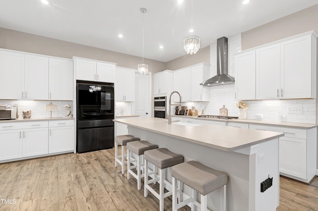 kitchen featuring wall chimney range hood, stainless steel appliances, an island with sink, and white cabinets