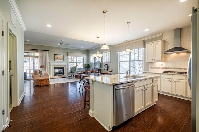 kitchen featuring sink, appliances with stainless steel finishes, light stone counters, a center island with sink, and wall chimney exhaust hood