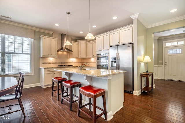 kitchen featuring decorative light fixtures, sink, stainless steel appliances, a center island with sink, and wall chimney exhaust hood