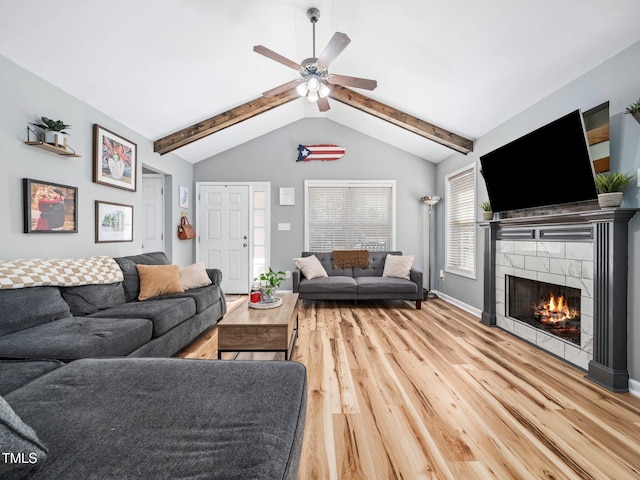 living room with a tile fireplace, vaulted ceiling with beams, hardwood / wood-style floors, and ceiling fan