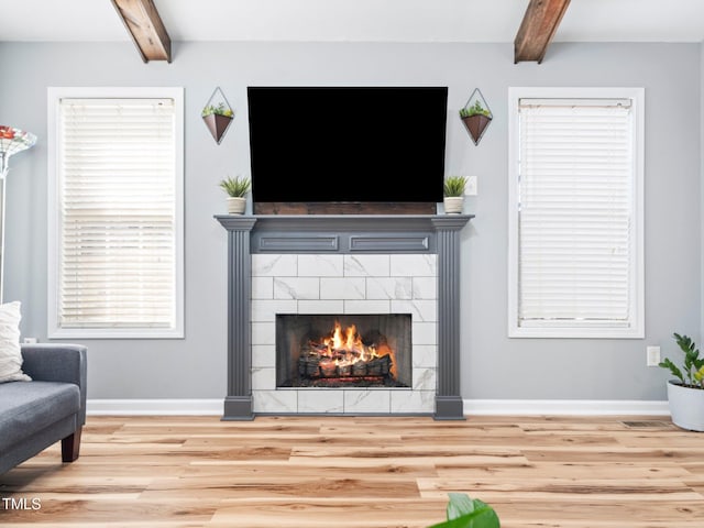 living room with beam ceiling, a tile fireplace, and light hardwood / wood-style flooring