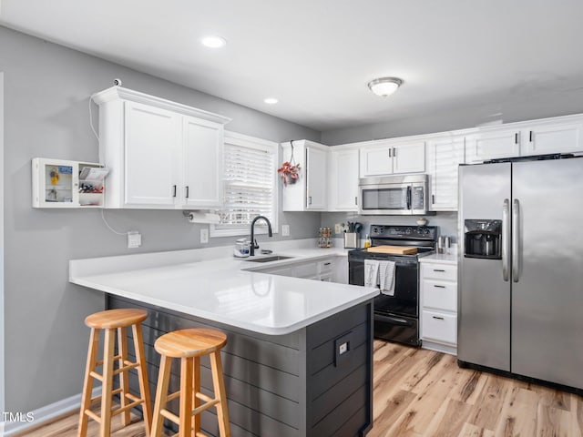 kitchen with appliances with stainless steel finishes, white cabinetry, sink, a kitchen breakfast bar, and kitchen peninsula